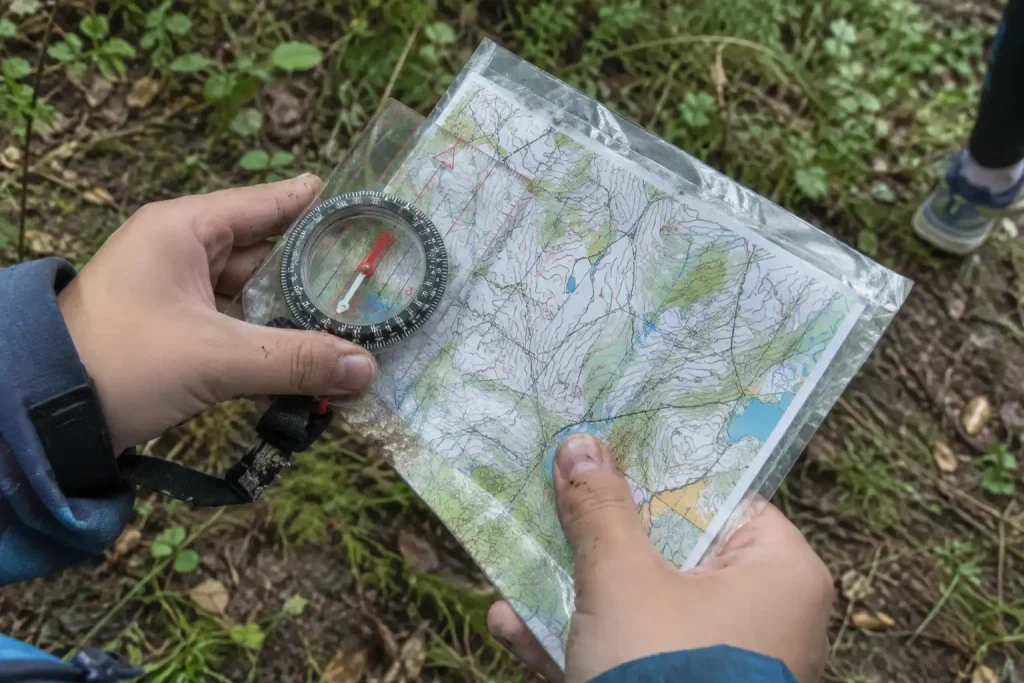 Barnhänder håller kompass och karta i skogen, ett exempel på varför orientering är med på skolidrotten