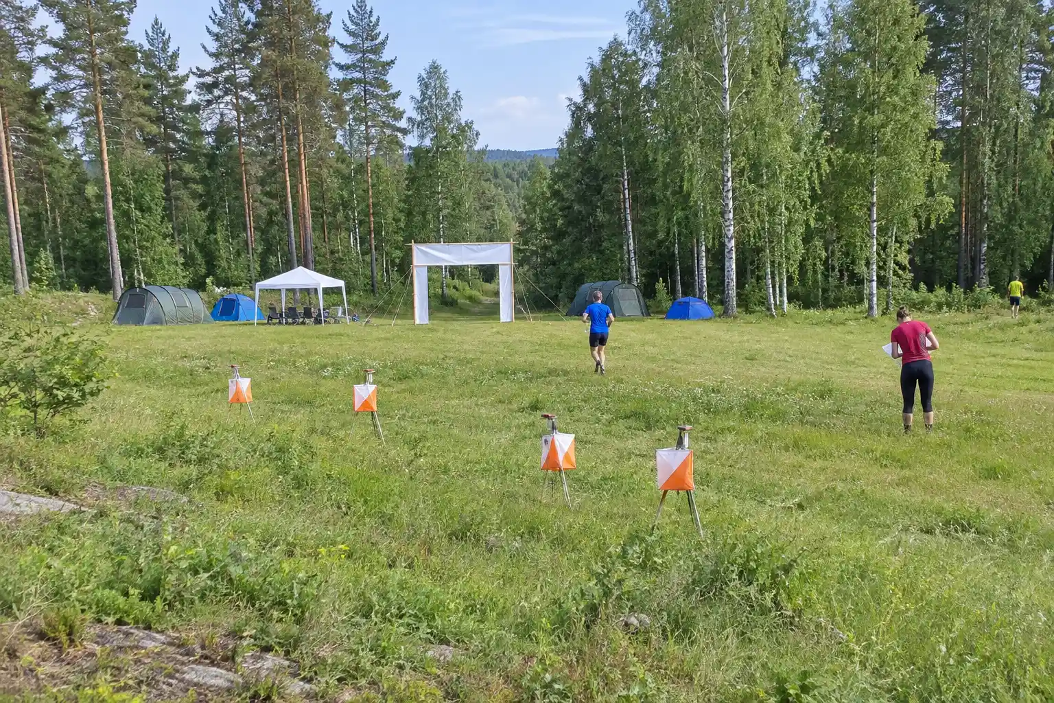 Orienteringskontroller och tält i en solbelyst glänta vid o-ringen i juli
