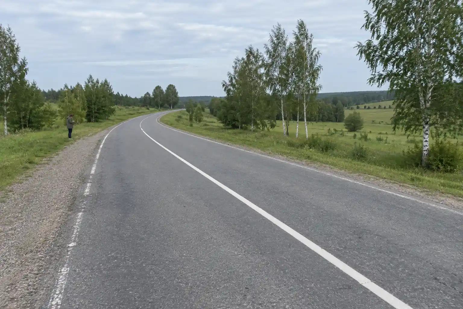 Lantlig landsväg med en heldragen linje som leder mot en kurva genom gröna fält